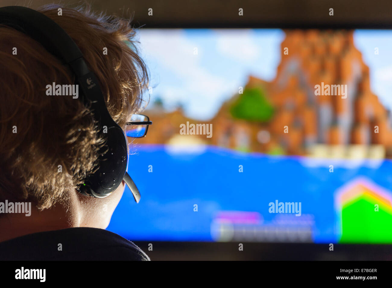 Un adolescente se sienta delante de la pantalla de su ordenador y juega el juego de ordenador Minecraft, desarrollado por la compañía sueca Mojang Foto de stock
