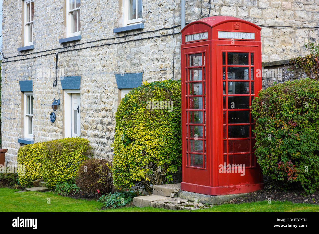 Rojo tradicional cuadro teléfono británica UK la cabina de teléfono al lado de una carretera con casas en segundo plano; Nunnington North Yorkshire Foto de stock