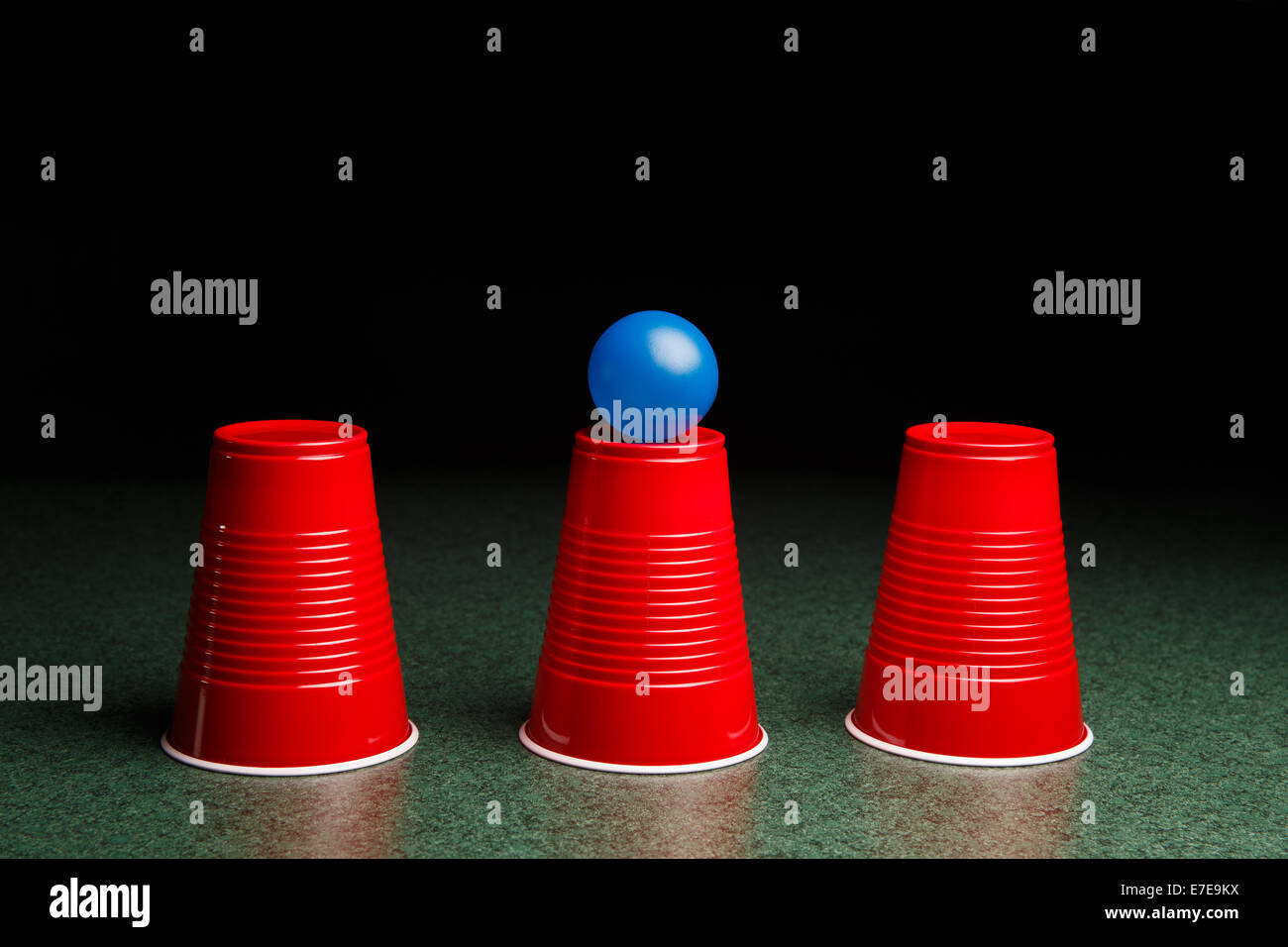 Juego de conchas - tres tazas de color rojo y una bola azul en un cuadro  verde dispuestos como el juego de conchas. Los juegos de azar. Copie el  espacio Fotografía de