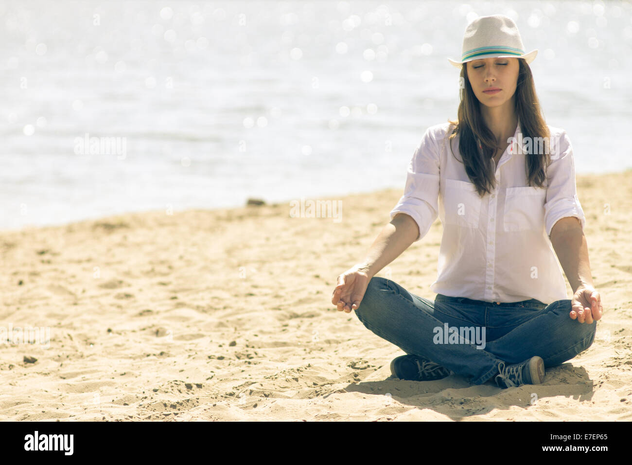 Joven en white hat relajarse en la playa en verano a mediodía. Hipster chica en meditación cerca del mar Foto de stock