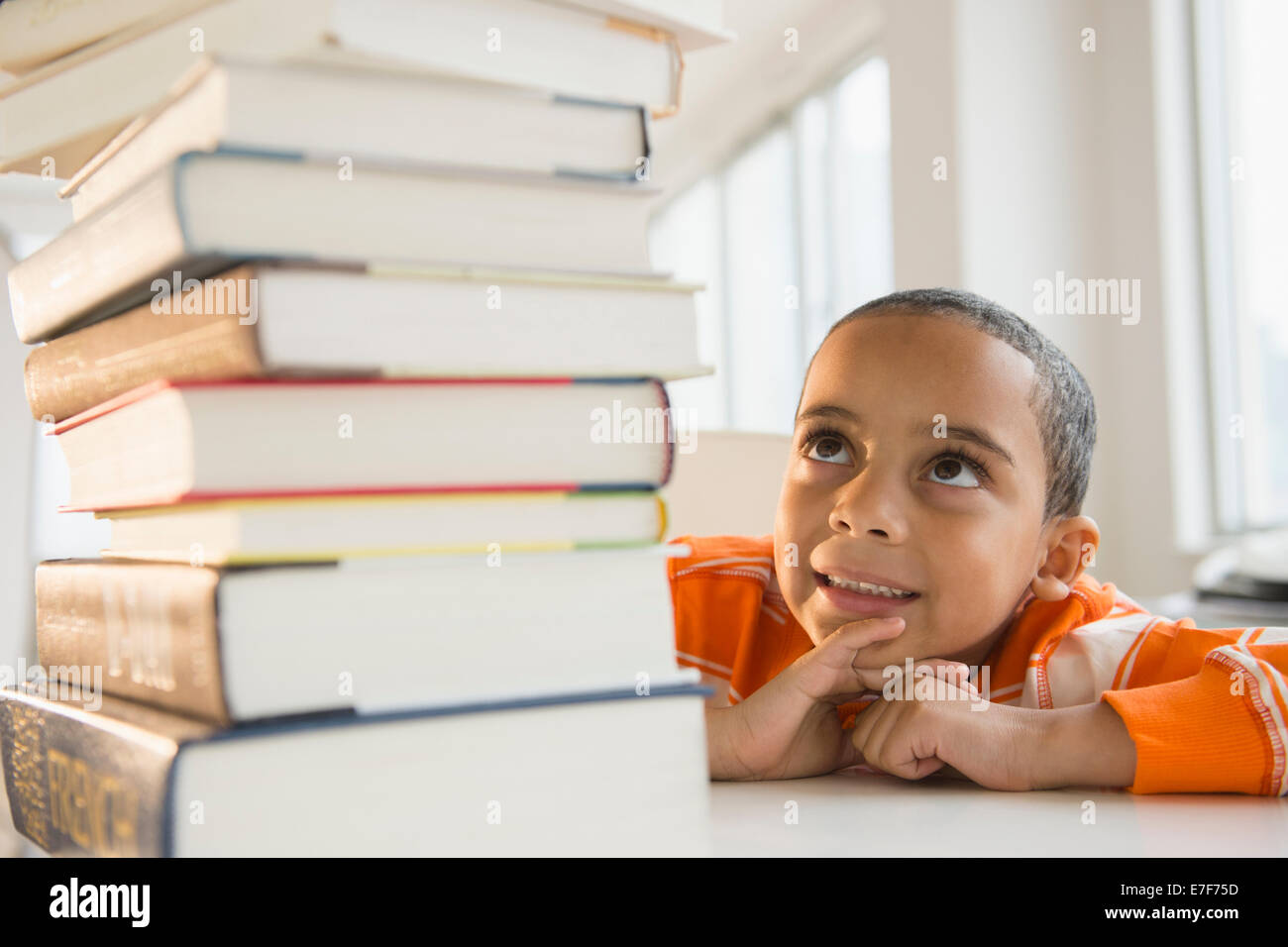 Mestizos niño mirando hacia arriba en la pila de libros Foto de stock