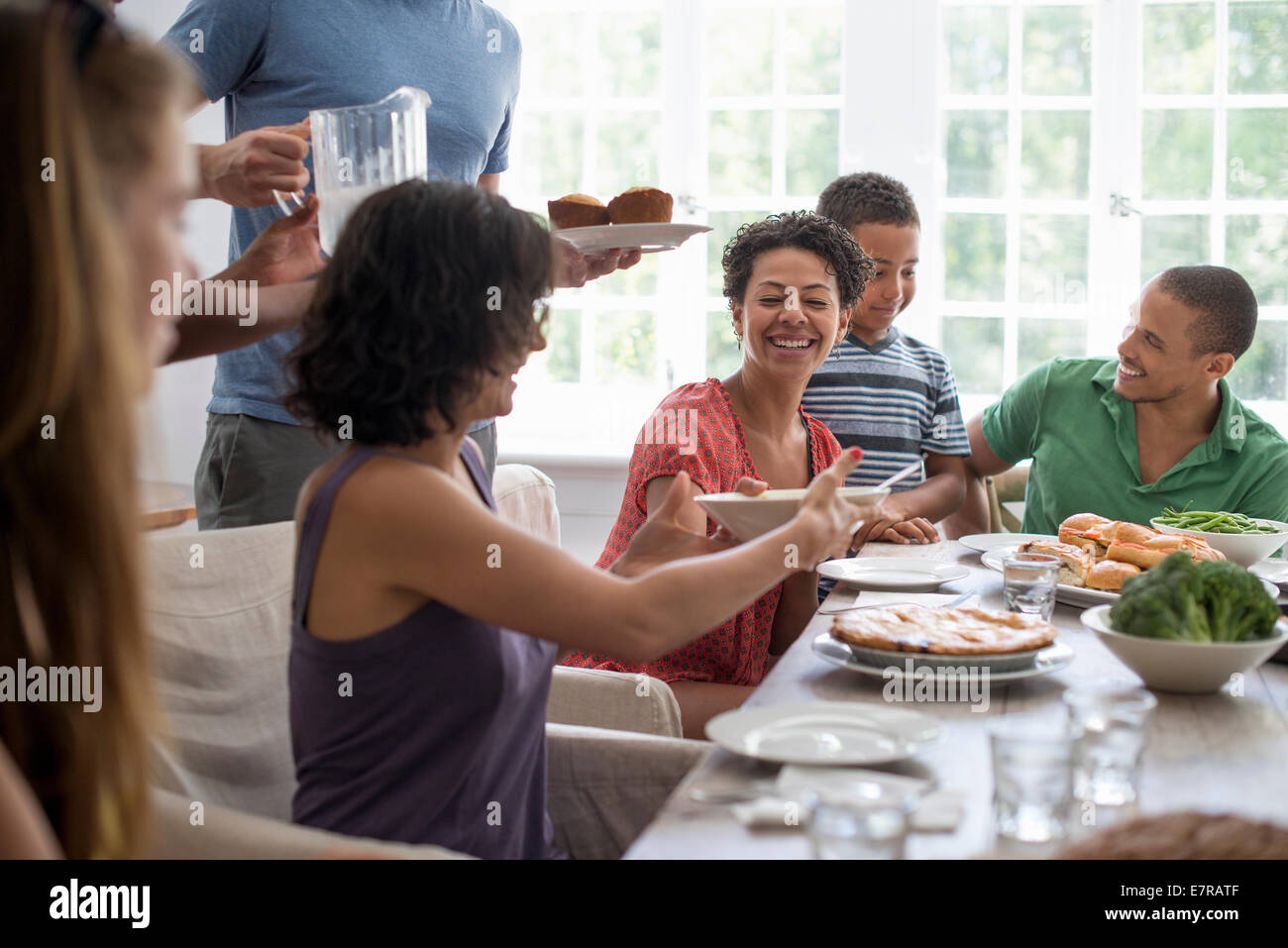 Una reunión familiar, hombres, mujeres y niños alrededor de una mesa de comedor de compartir una comida. Foto de stock