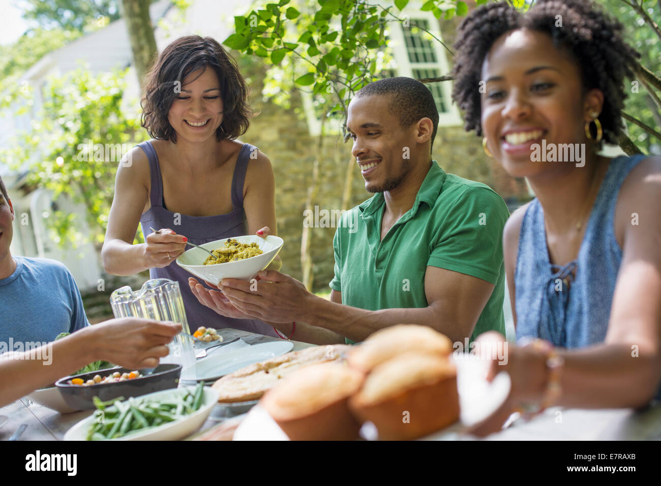 Una reunión familiar, hombres, mujeres y niños alrededor de una mesa en el jardín en verano. Foto de stock