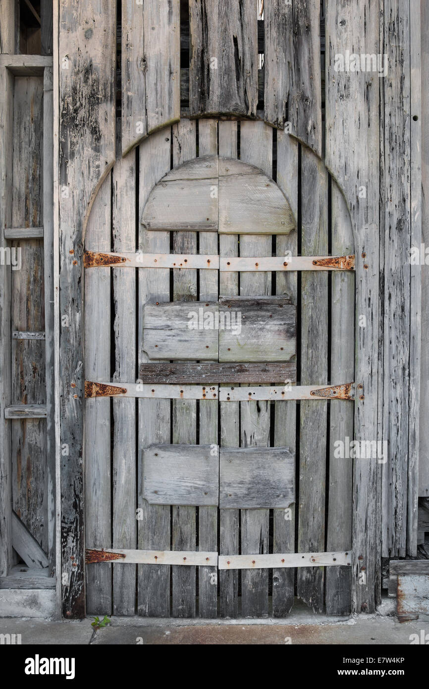 Rusty gris antiguas no usados abandonados driftwood arqueado de madera con doble puerta con agujeros y lagunas curtida por playa Foto de stock