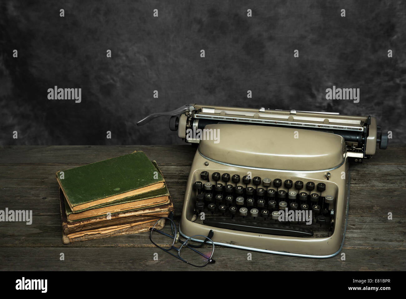 Máquina de escribir, libros y gafas de lectura en un sucio escritorio Foto de stock