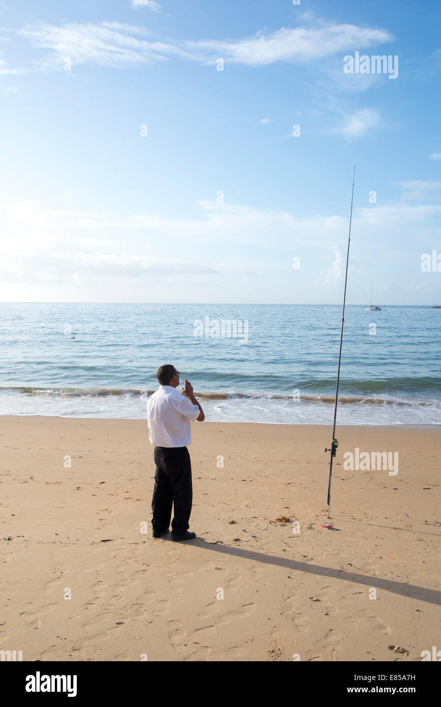 Hombre de pie en la playa de Cascais en pantalón negro y camisa blanca con  caña de pescar, a metros del restaurante de pescado trabaja Fotografía de  stock - Alamy