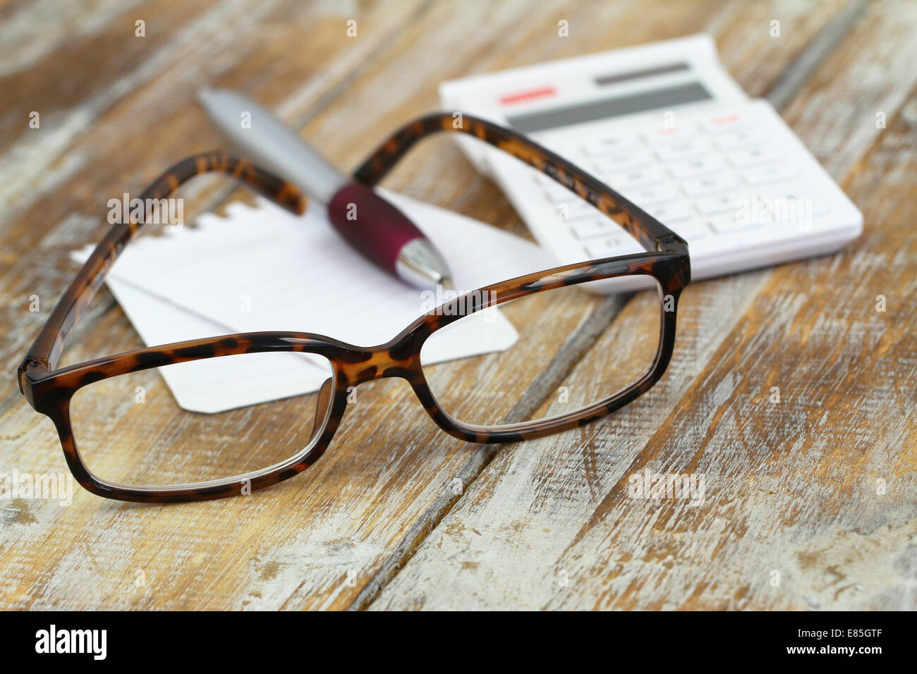 Gafas de lectura, calculadora, lápiz y papel de notas sobre la superficie de madera Foto de stock