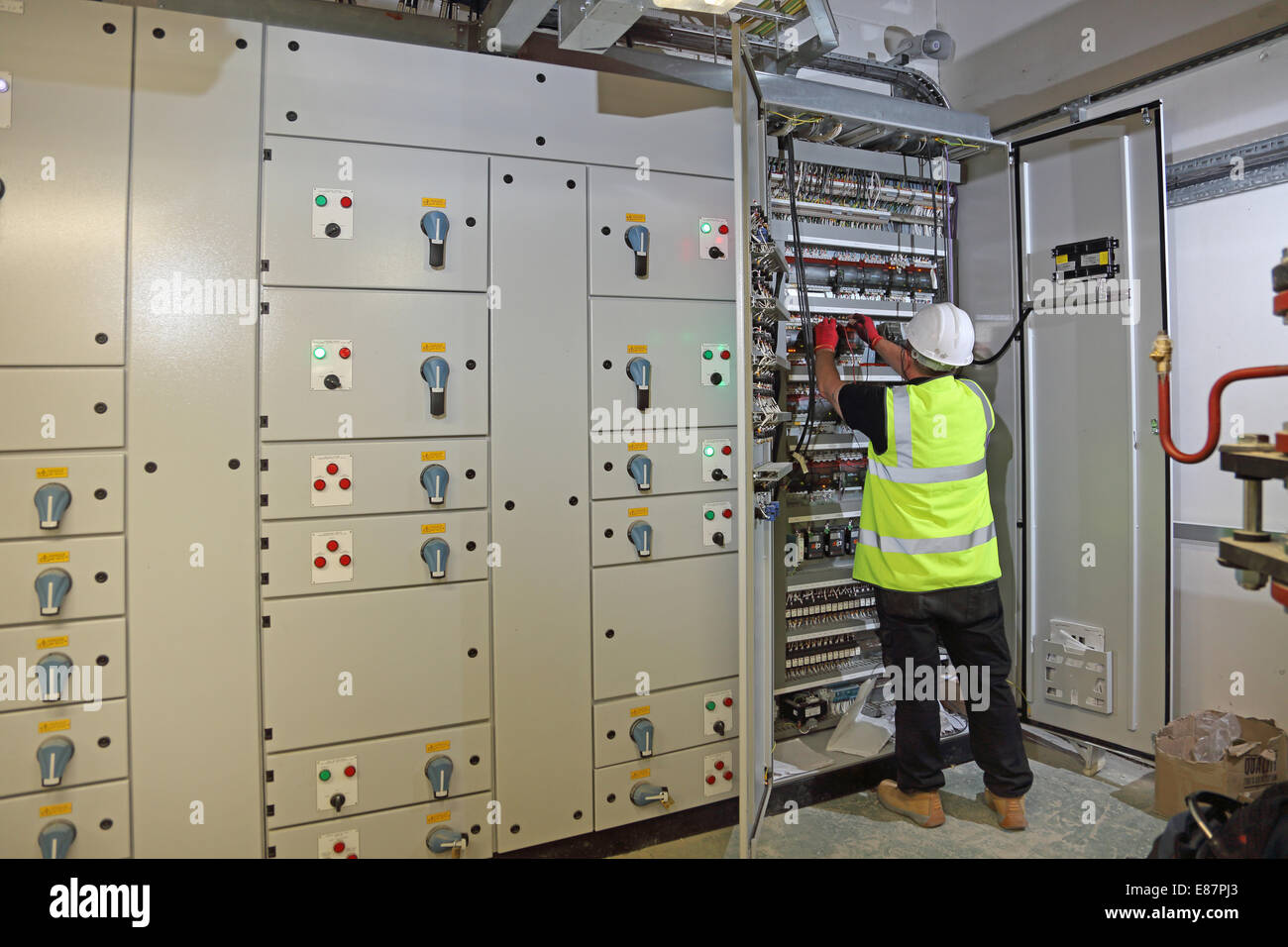 Un edificio servicios ingeniero trabaja en un armario de control eléctrico en la sala de la planta de un gran edificio de oficinas Foto de stock