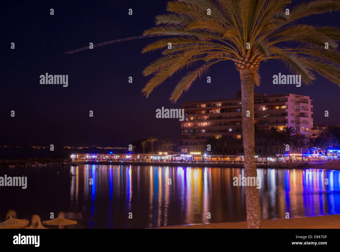 Escena nocturna Cala Estancia con luces de neón en la bahía y la línea aérea despegó desde el aeropuerto de Palma visto como puntos en el cielo. Foto de stock