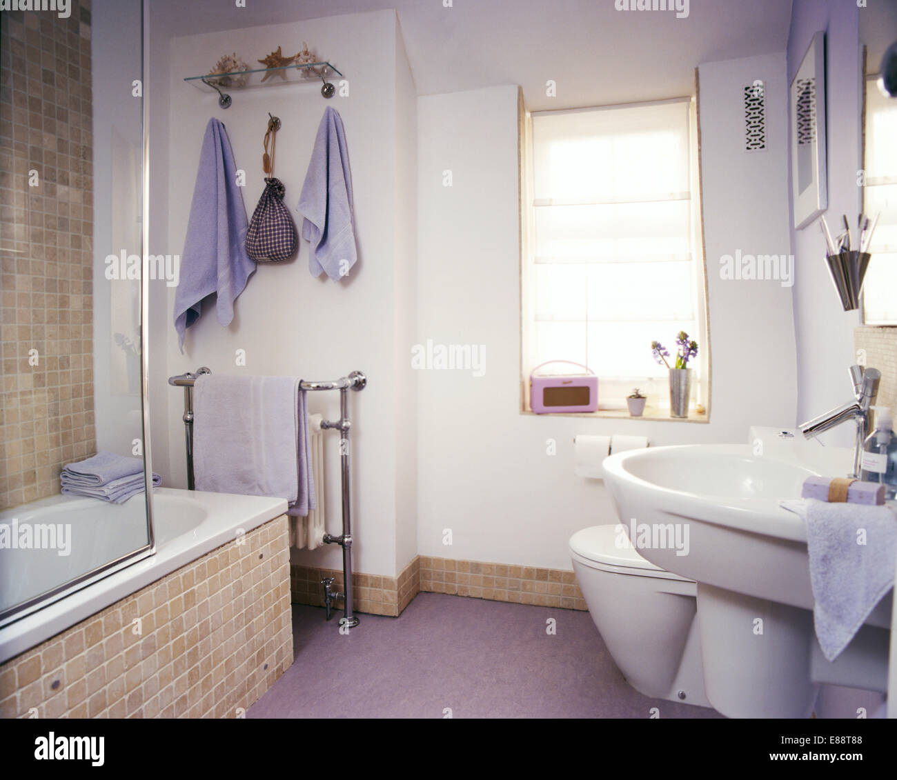Baño con mosaicos de color beige surround y rodapié en el moderno cuarto de  baño con toallas de color malva y rosa Roberts radio Fotografía de stock -  Alamy