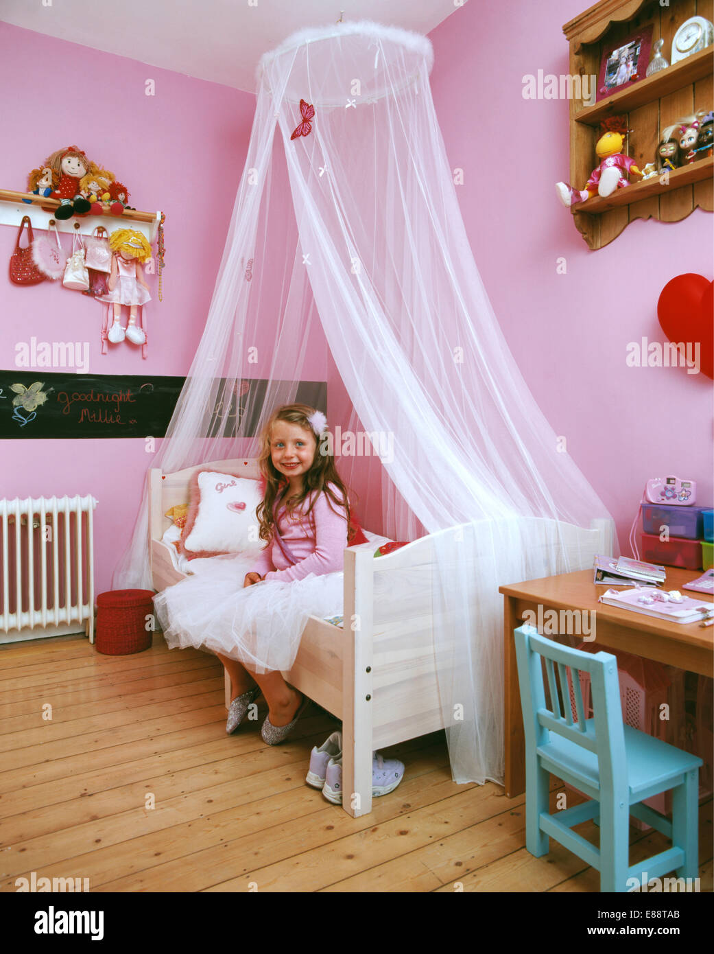 La pequeña niña sonriente sentada en la cama con cortinas de velo blanco en  rosa del niño dormitorio sólo para uso editorial Fotografía de stock - Alamy