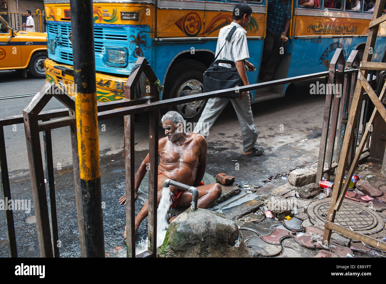 Un hombre toma un baño público en una concurrida calle en Calcuta, India. Foto de stock