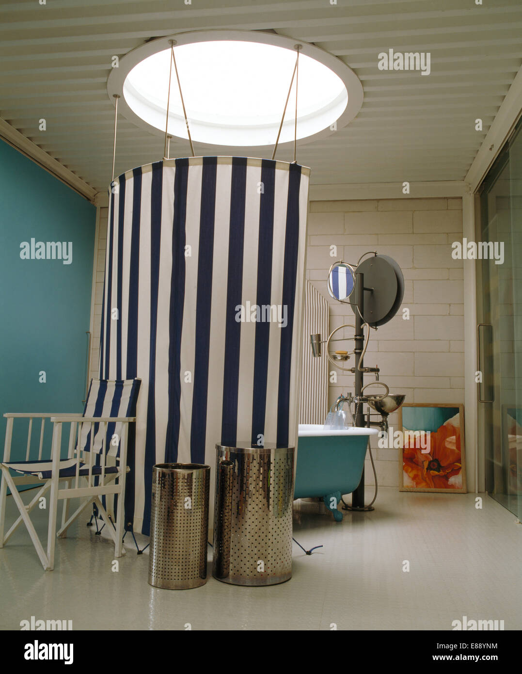 Los recipientes metálicos y silla del director junto a negro+blanco rayado cortina de lona alrededor de ducha en el cuarto de baño moderno Foto de stock
