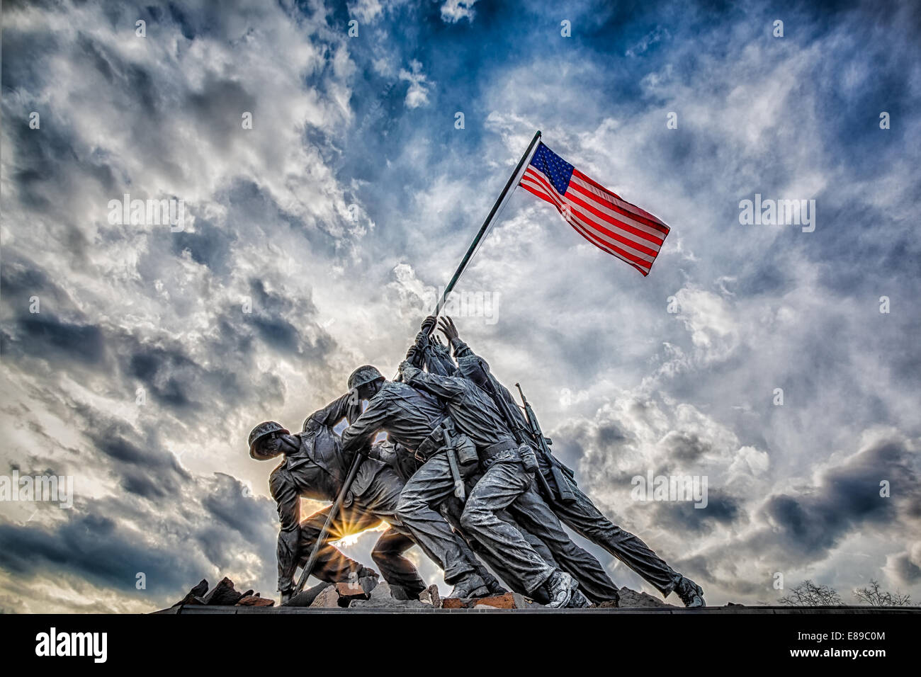 El Marine Corps War Memorial también llamado el Iwo Jima Memorial en Arlington, Virginia, con dramáticas nubes de tormenta en el fondo y un destello al atardecer. Foto de stock