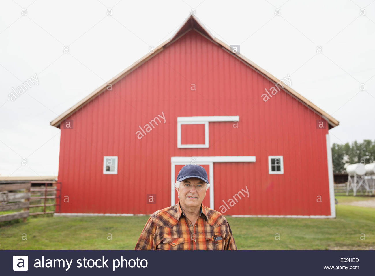 Agricultor de pie delante del granero rojo Foto de stock