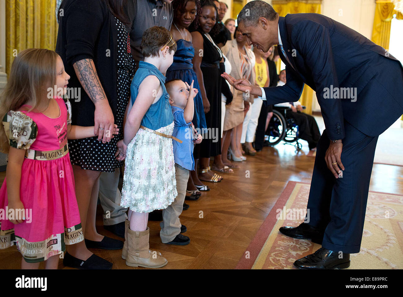 El presidente Barack Obama tiene hasta tres dedos mientras habla con tres-año-viejo Holden Fossum y sus hermanas Ayla, 8 y Alejandría, 4, durante un saludo con guerreros heridos y sus familias en el East Room de la Casa Blanca, 14 de julio de 2014. Holden, un Foto de stock