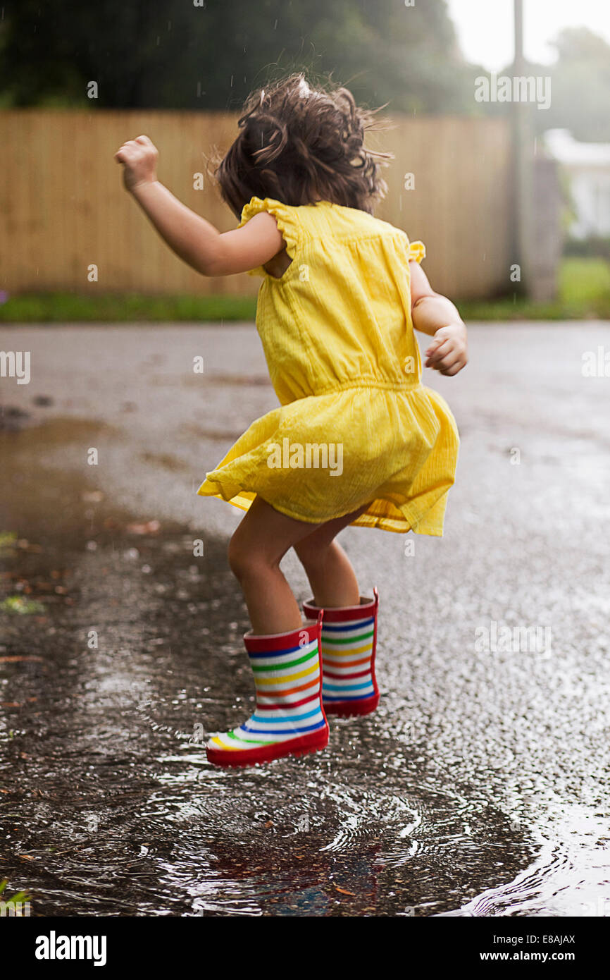 Chica usando botas de goma de saltar en charcos de lluvia Foto de stock