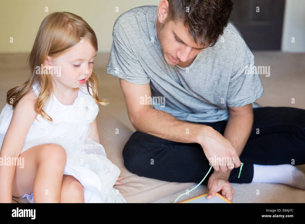 Joven e hija enhebrado de libro ilustrado en salón. Foto de stock