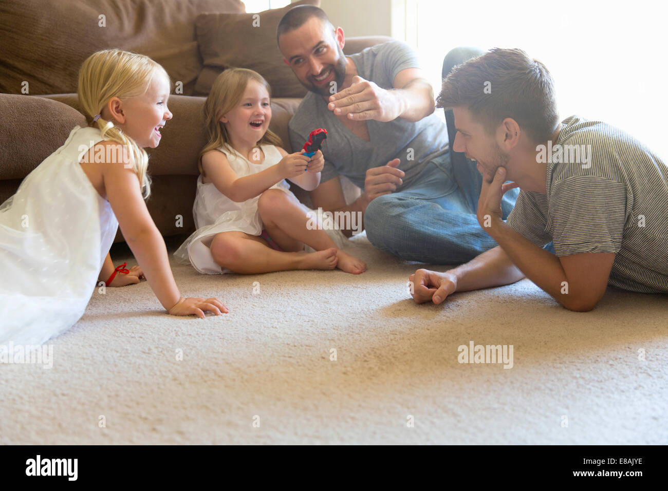 La pareja masculina y dos hijas jugando en el suelo de la sala de estar Foto de stock