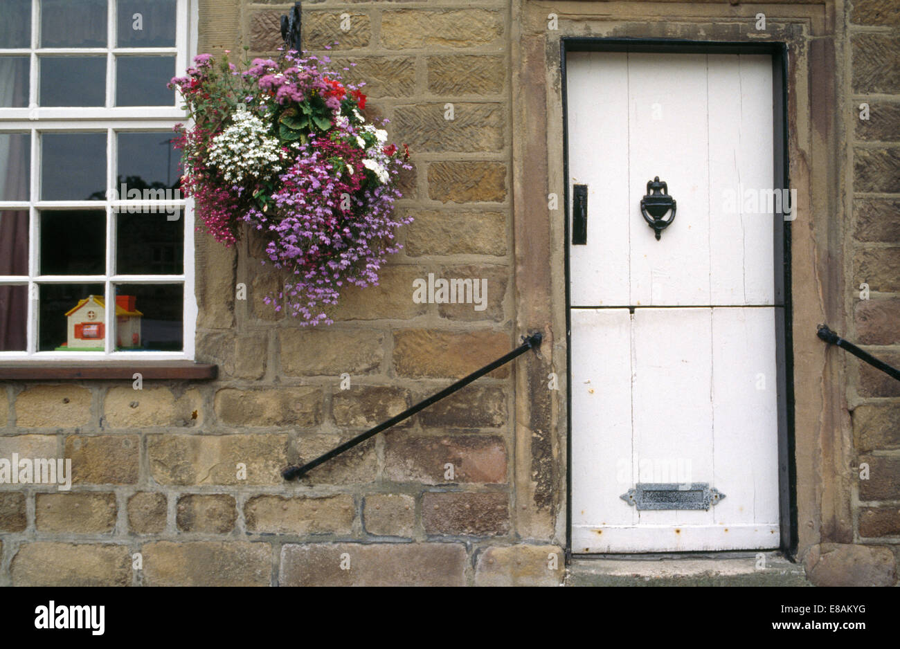 Geranios en cestas colgantes al lado de la puerta delantera blanca de casa en piedra con barandillas en las paredes. Foto de stock