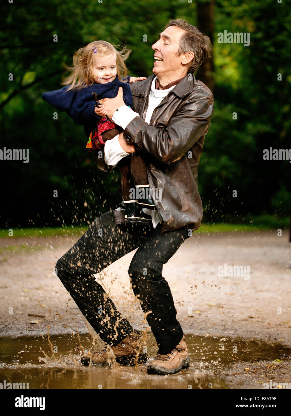Celebración Padre hija, salpicando en charco Foto de stock