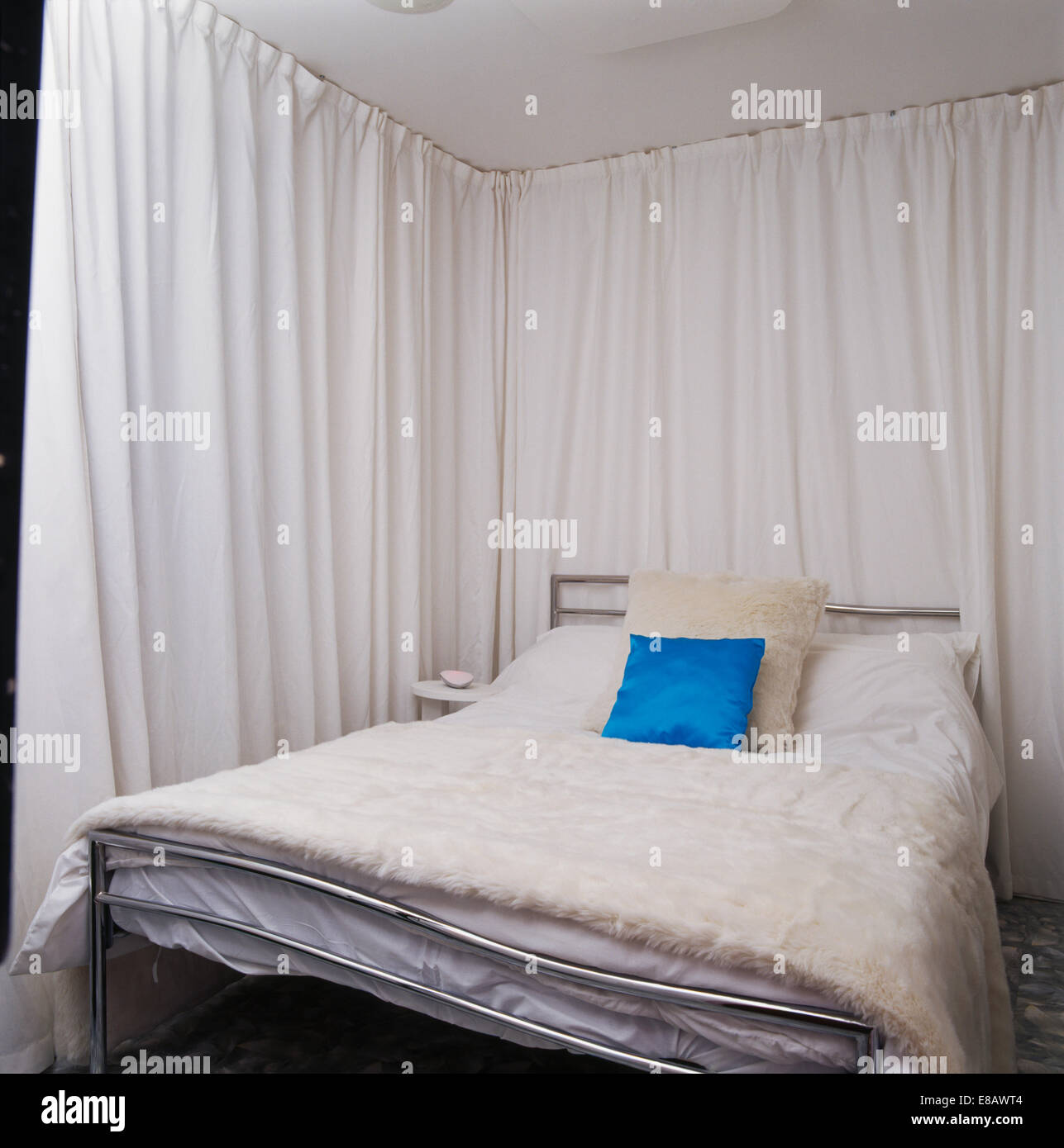 Cortinas blancas en las paredes de la economía-estilo dormitorio con cama  de piel falsa blanca-cubierta en la cama de metal Fotografía de stock -  Alamy