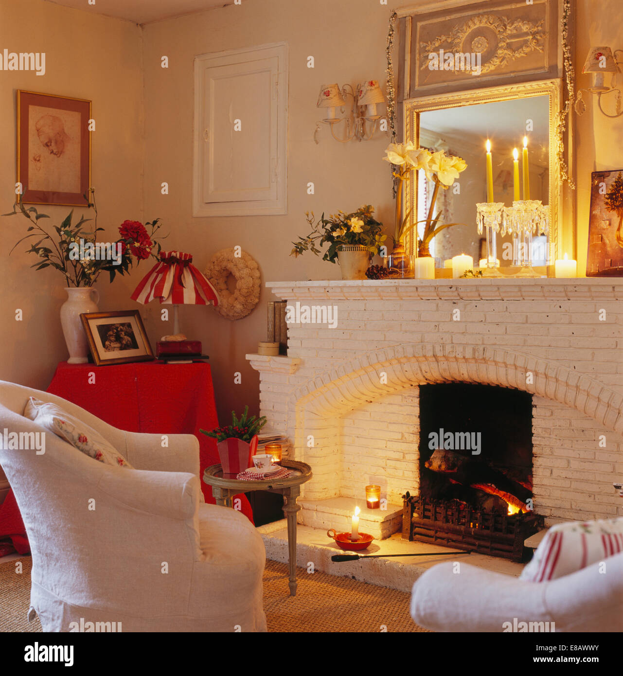 Espejo en la pared sobre la chimenea con velas encendidas en la sala de  estar con sillones de color crema en frente de la chimenea Fotografía de  stock - Alamy