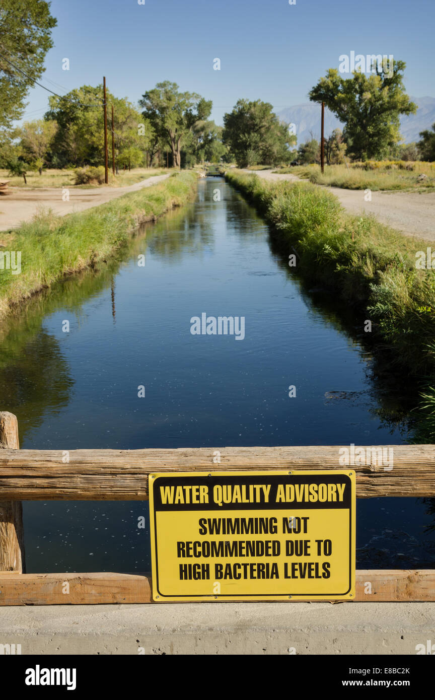 Signo de asesoramiento de calidad del agua advertencia contra nadar en un canal de riego debido a altos niveles de bacterias Foto de stock