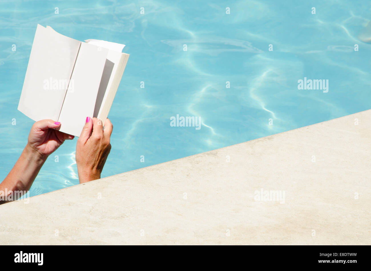 Leer un libro junto a la piscina con una bebida fría en los calurosos días de verano. Foto de stock