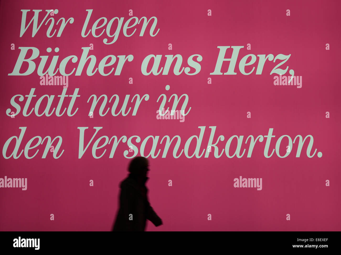 Una mujer camina más allá de un muro iluminado diciendo "Wir legen Bücher ans Herz, statt nur in den Versandkarton" (engl. "Queremos poner libros en su corazón, en lugar de sólo la caja de transporte"), en el stand de la feria Boersenvereins des Deutschen Buchhandels (Asociación Alemana de editores y libreros) en la feria del libro de Frankfurt/Main (Hesse), Alemania, el 06 de octubre de 2014. El anuncio es parte de la iniciativa de la industria alemana del libro "Vorsicht Buch" (engl. Libro 'Atención'). El libro de la exposición más grande del mundo tiene lugar desde el 08 de octubre hasta el 12 de octubre de 2014. Finlandia es el anfitrión de este año cou Foto de stock