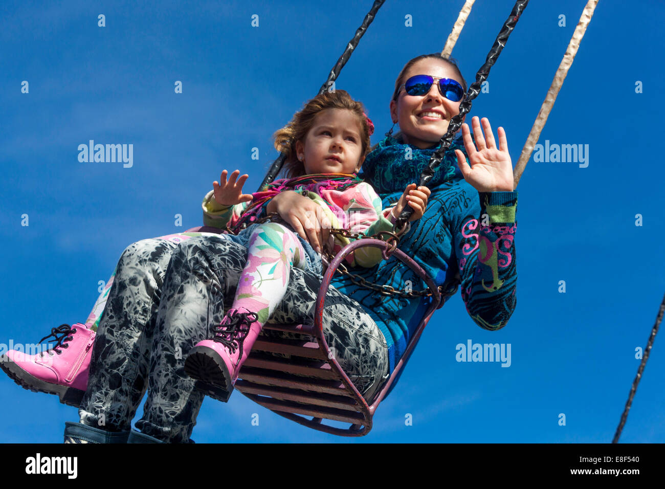 Madre con hija disfrutando de la vida en la cadena de carrusel swing, parque de atracciones feliz familia Foto de stock