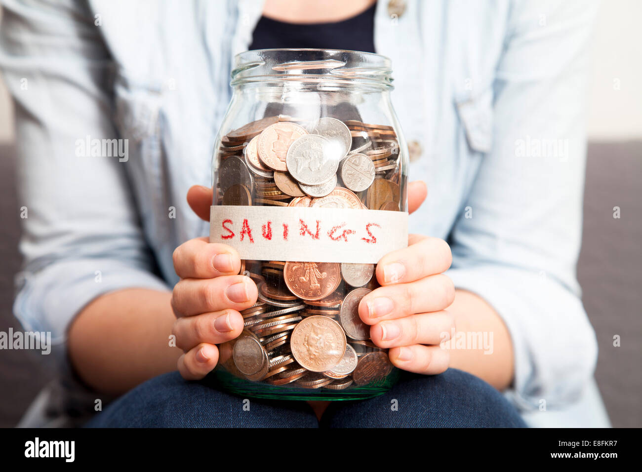 Primer plano de una mujer sosteniendo un tarro de ahorros lleno de monedas Foto de stock