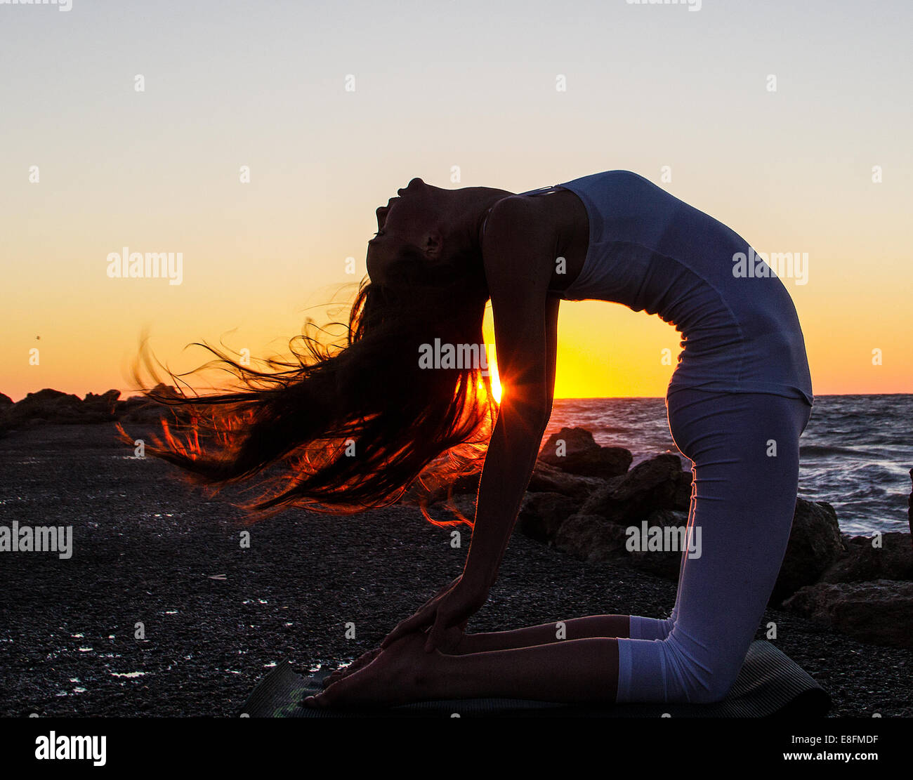 Mujer practicando yoga en la playa en el atardecer. Foto de stock
