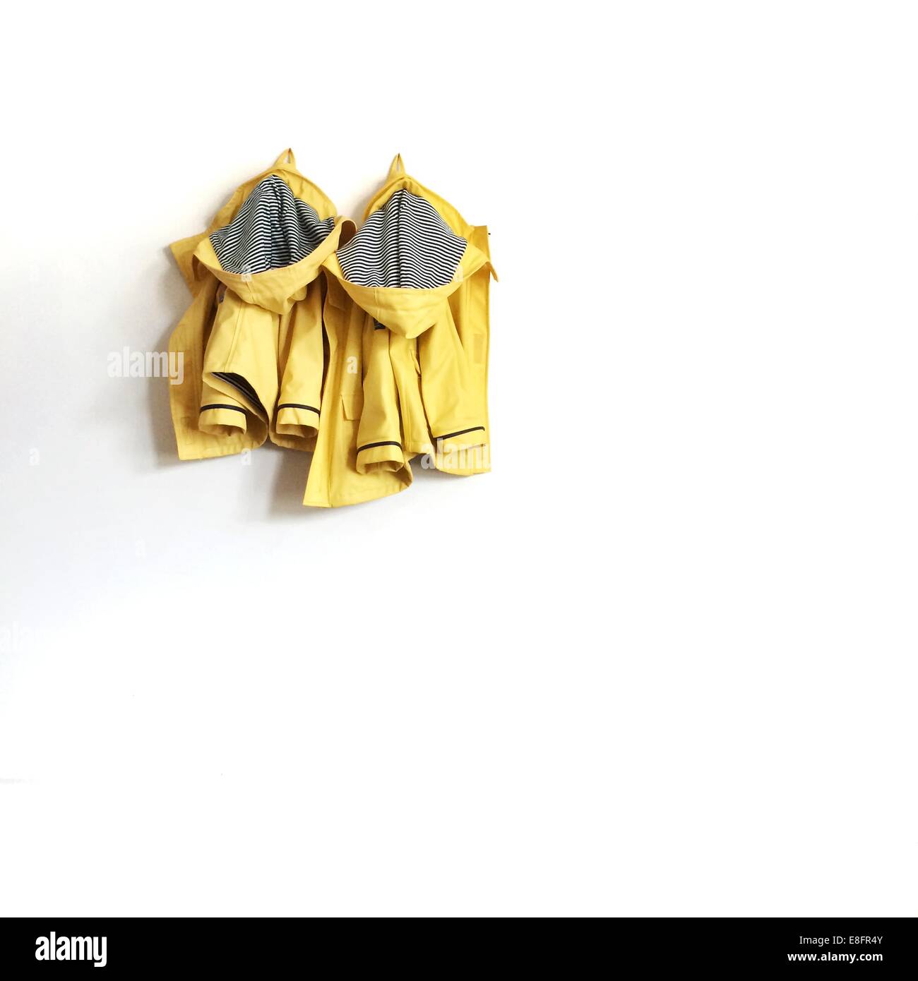 Dos impermeables amarillos colgando de la pared Foto de stock
