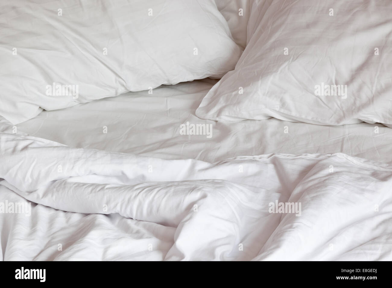 Cómoda, Cama desordenada con almohadas y edredón Foto de stock