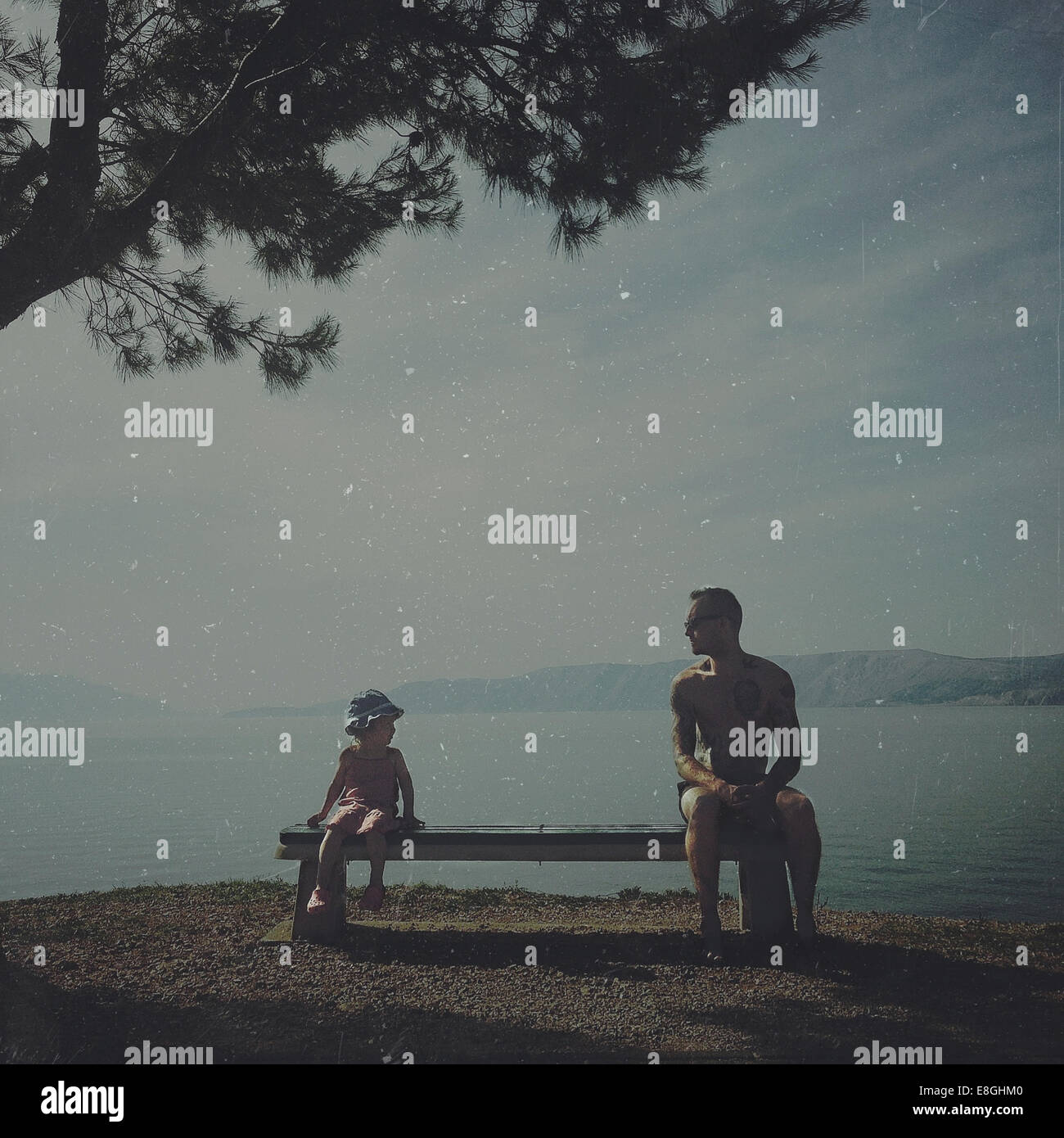 Padre e hija sentados en un banco junto al mar, Croacia Foto de stock