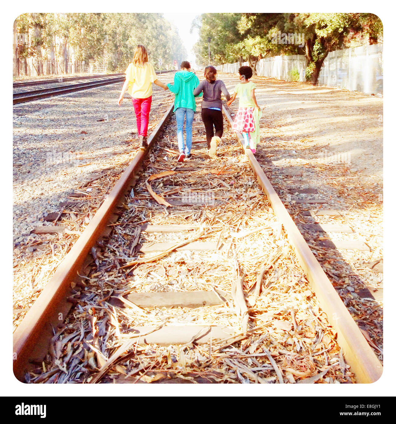 Cuatro niños caminando por vías de ferrocarril abandonadas con las manos, California, Estados Unidos Foto de stock