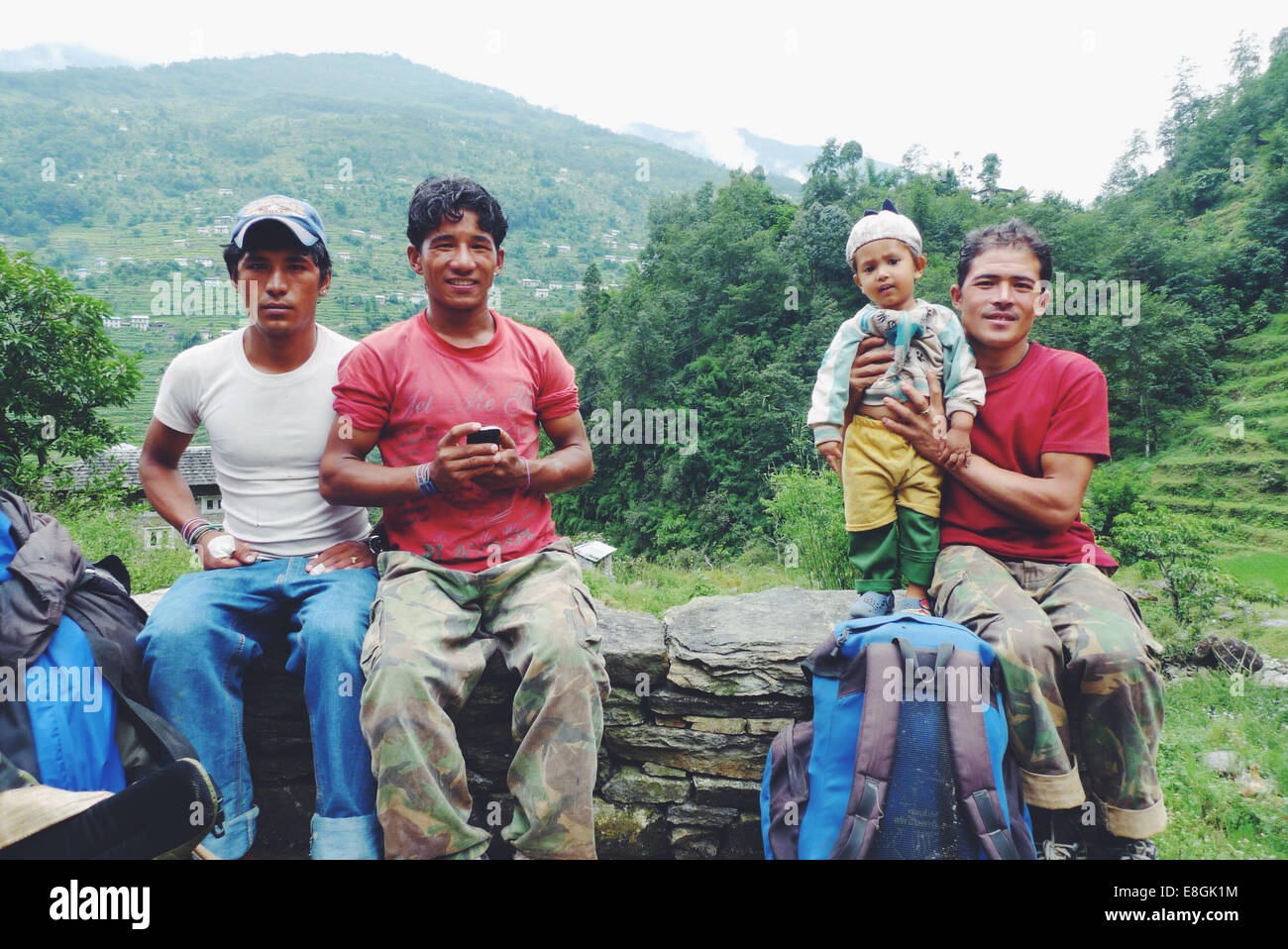 Tres hombres nepaleses sentados en una pared con un niño, Nepal Foto de stock