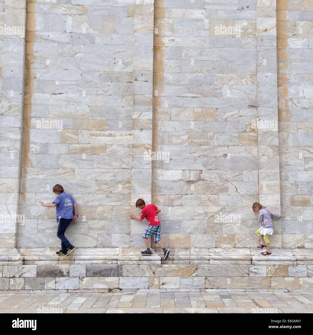 Tres niños caminando a lo largo de una pared de ladrillo, Pisa, Toscana, italia Foto de stock