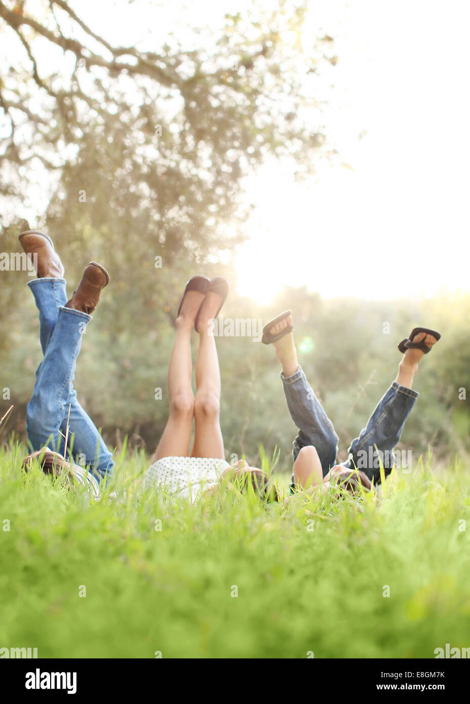Tres niños tumbados en la hierba con las piernas en el aire Foto de stock