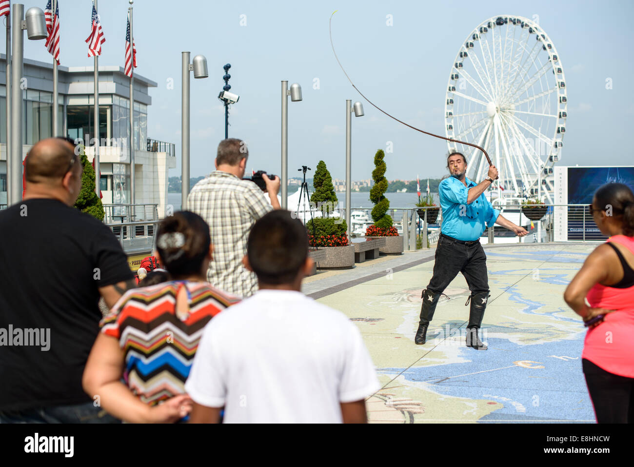 Un vaquero street performer grietas un látigo en National Harbor en  Maryland, sobre la orilla del Potomac cerca de Washington DC. En el fondo  es la noria gigante Fotografía de stock -