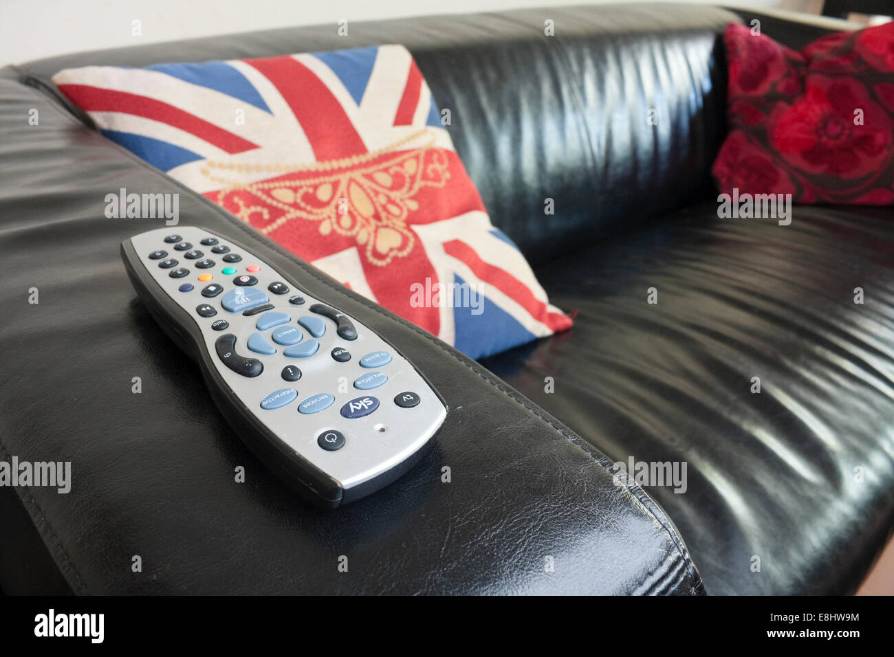 Un mando a distancia de televisión satelital Sky en el brazo de un sofá de cuero negro. Foto de stock