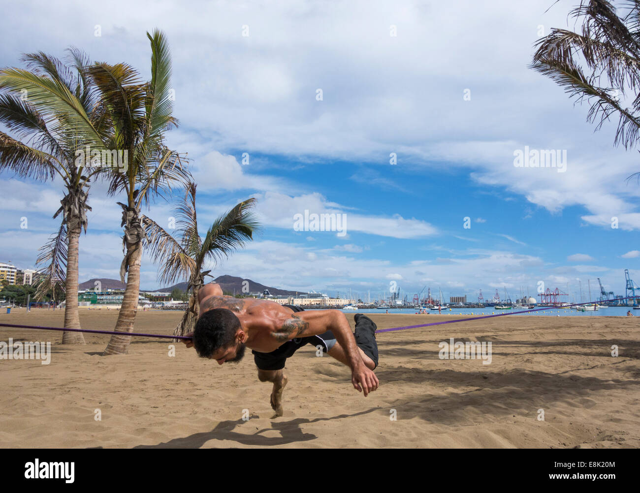 El hombre realizar volteretas y gimnasia desmonta en slackline atadas entre árboles de Plam Beach en España Foto de stock
