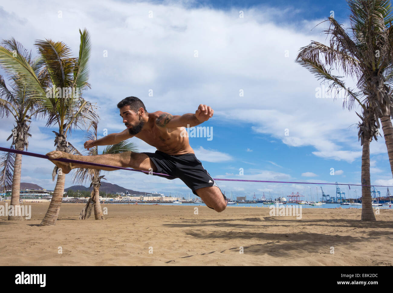 El hombre realizar volteretas y gimnasia desmonta en slackline atadas entre árboles de Plam Beach en España Foto de stock