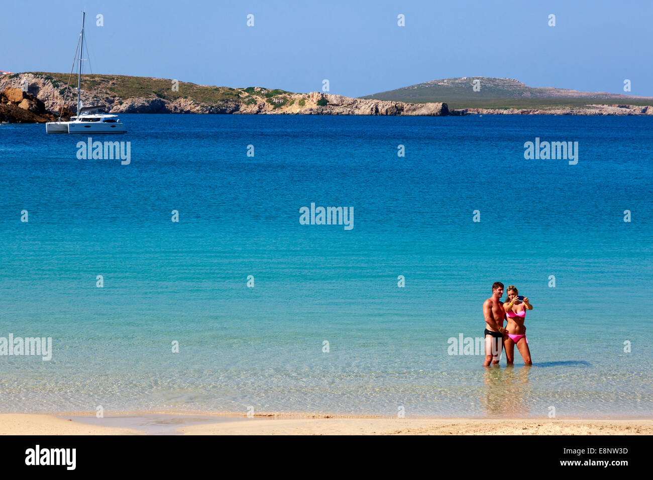El hombre y la mujer de vacaciones teniendo una 'fotografía' elfie mientras está de pie en el mar en Arenal d'en Castell, Menorca, España Foto de stock