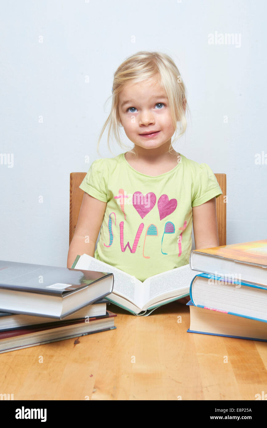 Lindo niño joven chica rubia leyendo y estudiando su libro, fondo blanco, pila de libros Foto de stock
