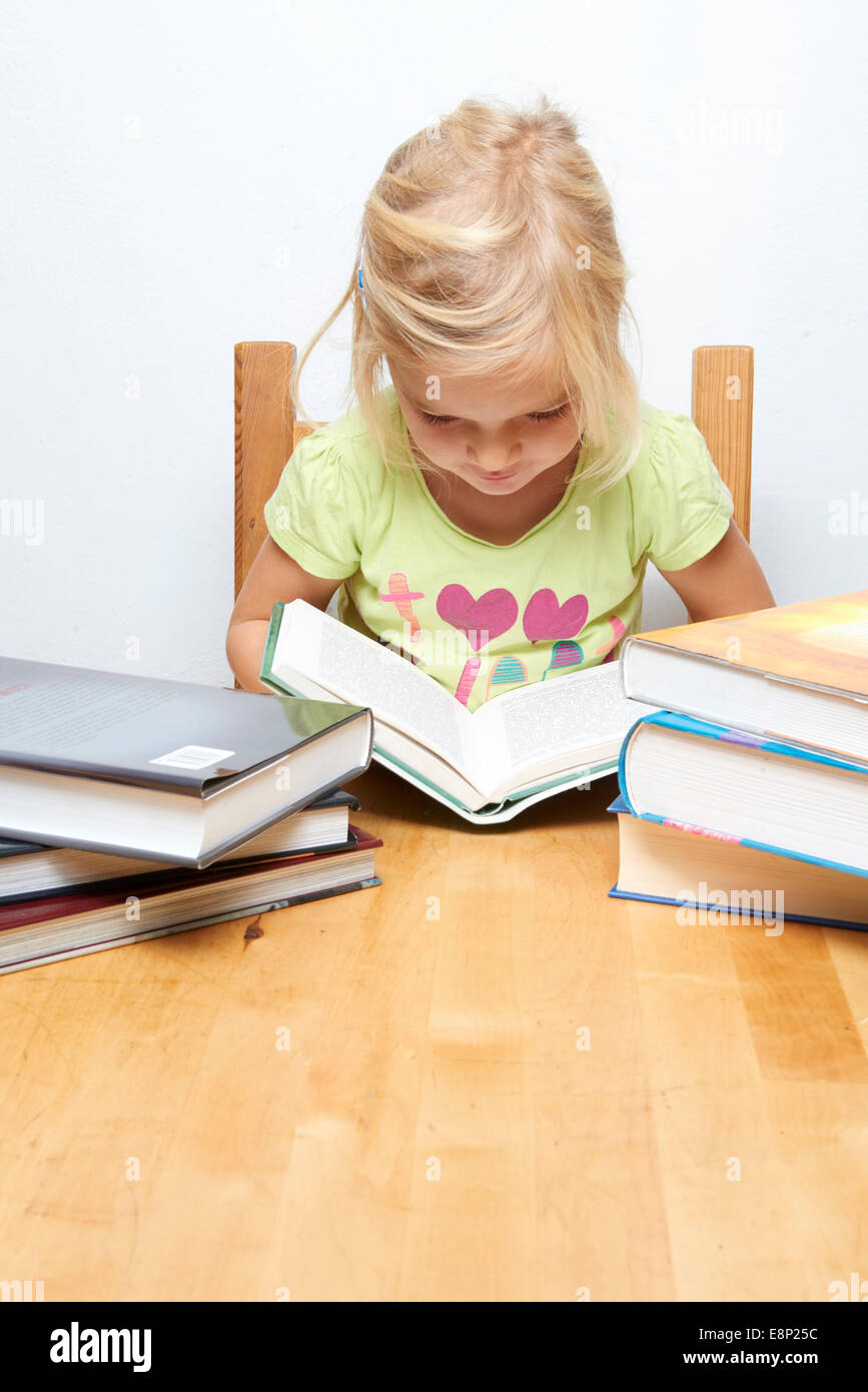 Lindo niño joven chica rubia leyendo y estudiando su libro, fondo blanco, pila de libros Foto de stock