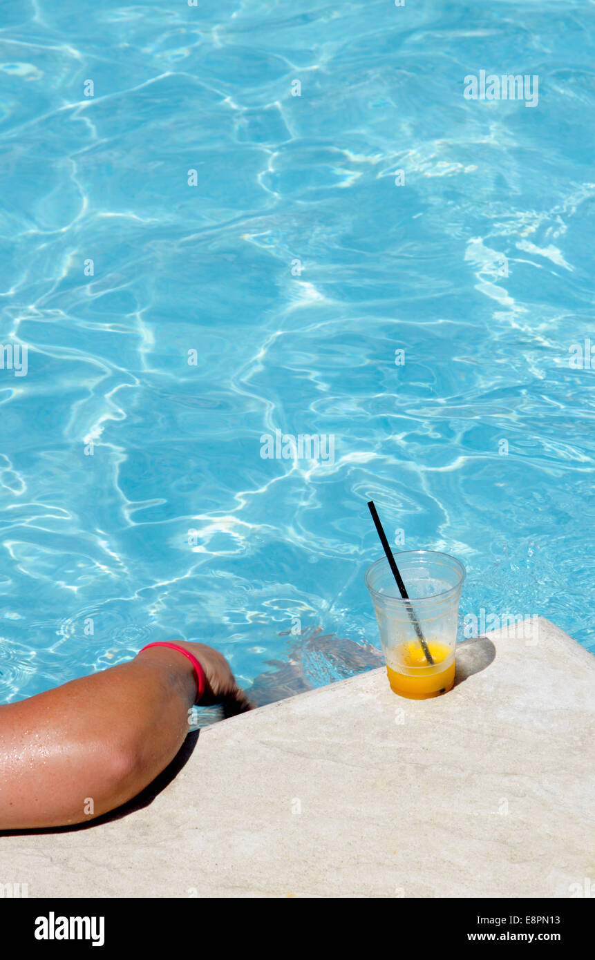 Leer un libro junto a la piscina con una bebida fría en los calurosos días de verano. Foto de stock