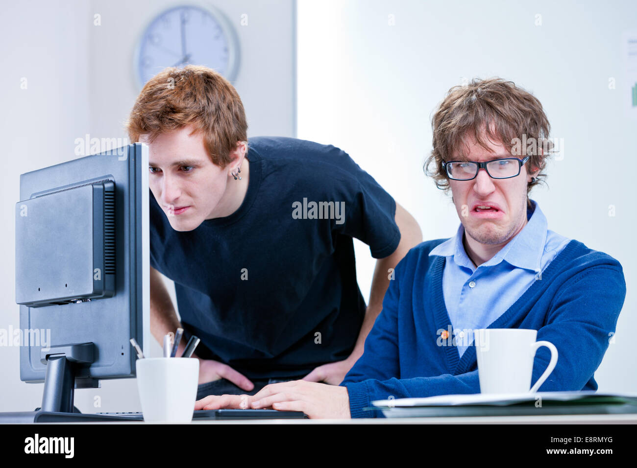 Un trabajador de oficina disgustado mientras el otro busca algo en una pantalla de ordenador Foto de stock