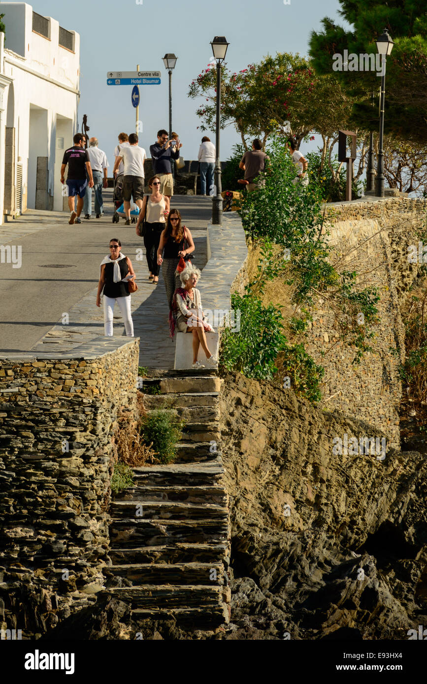 La gente disfruta de un paseo por el paseo marítimo durante una soleada tarde de verano en la ciudad de Cadaques. Foto de stock